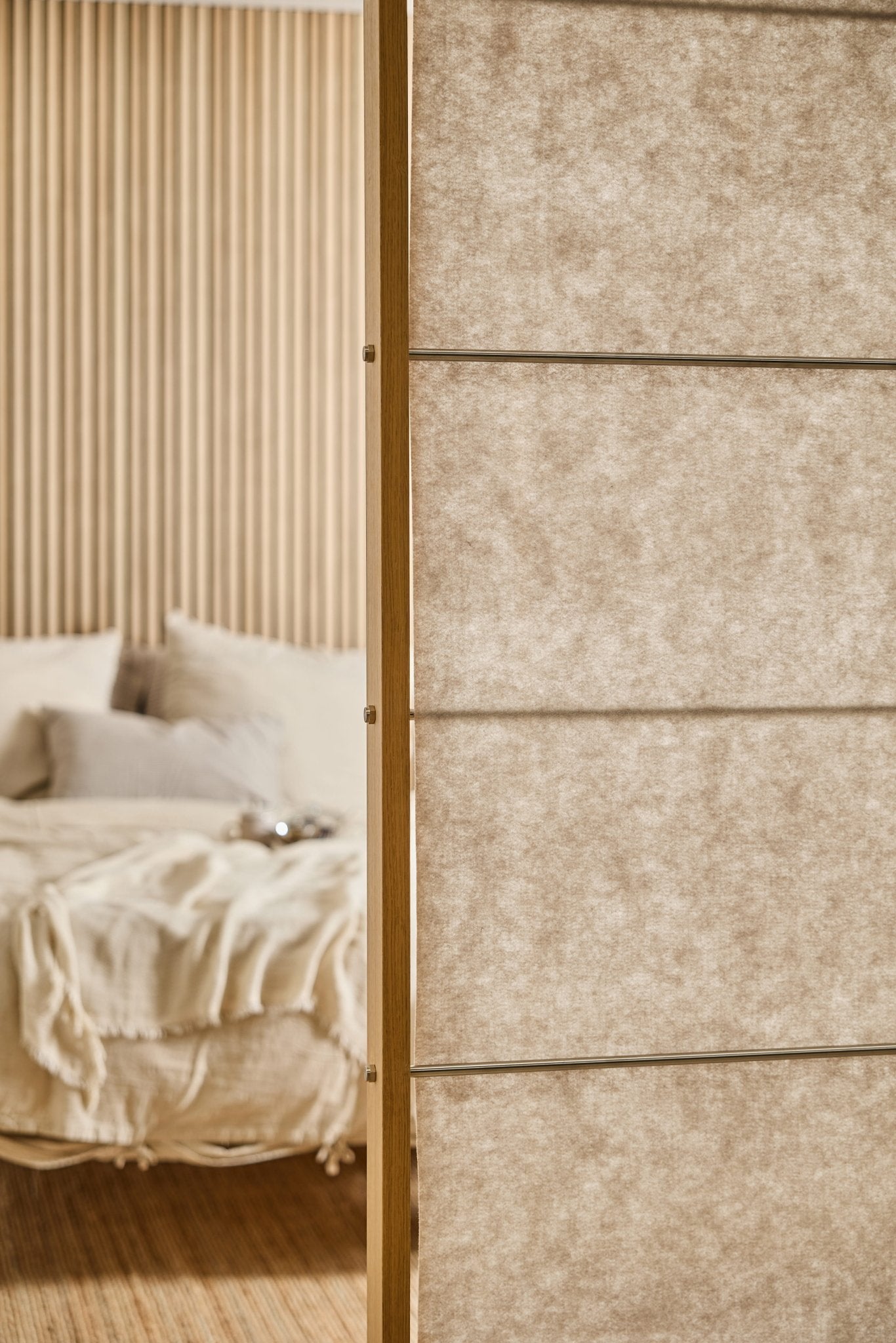 Camera da letto con un letto beige, una morbida coperta e un lenzuolo in feltro Vigg beige chiaro (58x241 cm); in primo piano, il divisorio EMBRACE di WoodUpp.